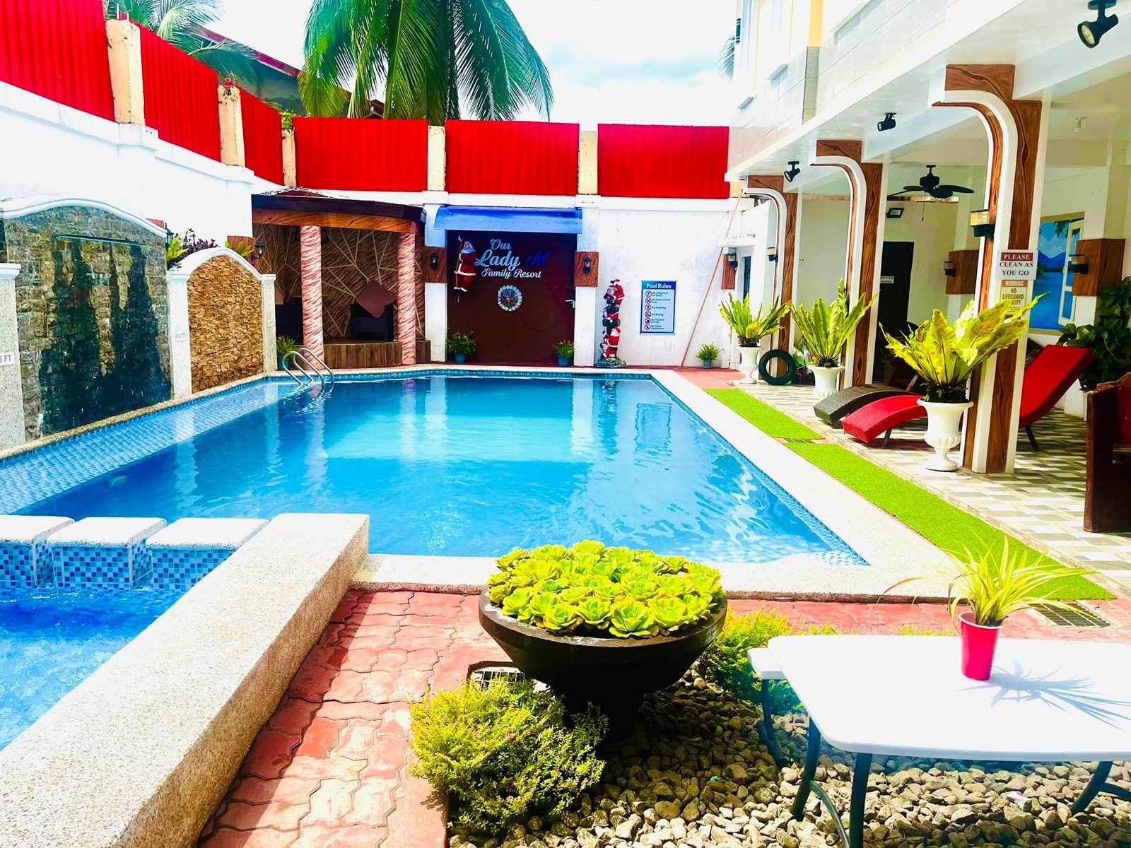 Bright blue pool with spa steps in front, sun loungers on the right and the resort sign in the back